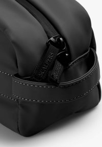 Bolsa zipper negra hecha de material mate. Presenta un zipper texturizado y una correa con costuras en contraste a lo largo de los bordes para mayor detalle.