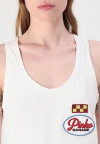 Witte tanktop met een wijde halslijn, voorzien van een rood en geel geruit patch en een geborduurd "Pinko GARAGE" patch.