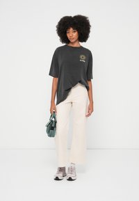 Szénszürke, túlméretezett póló napsütéses grafikával, krémszínű, bő szárú nadrág, rózsaszín tornacipő és zöldeskék kézitáska. Egyszerű, laza stílus.