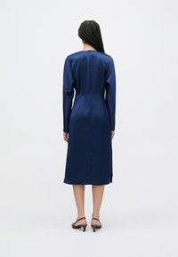 Tengerészkék szatén ruha hosszú ujjakkal, testhezálló felsőr�ésszel és közép hosszúságú szoknyával, hátul hasítékkal, sima textúrával és elegáns kivitelben.