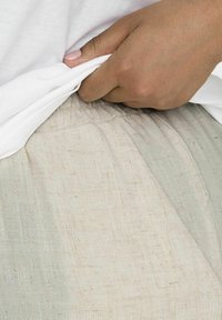 Lichtbeige linnen broek met een elastische tailleband, met een gestructureerd oppervlak; een deel van een wit overhemd is zichtbaar boven de tailleband.
