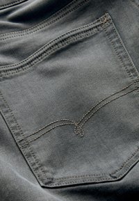 Grå denimstof med en baglomme, der har kontrastfarvet brun stikning og et buet designdetalje langs toppen.