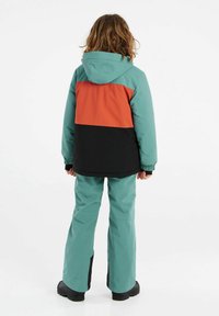 Completo invernale a due pezzi con giacca teal e arancione con dettagli neri e pantaloni teal dalla vestibilità ampia con pannelli laterali neri.