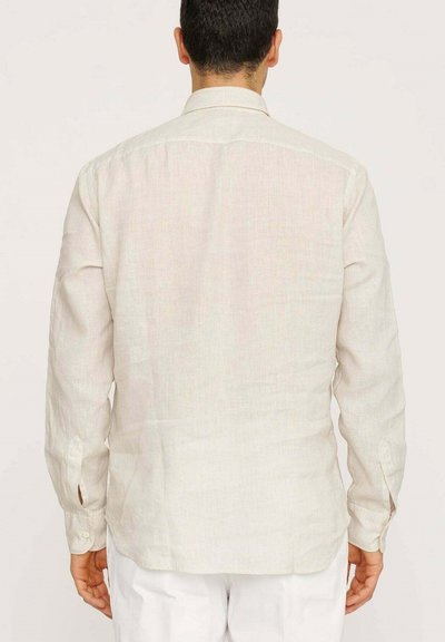 Camicia in lino color beige chiaro, vista posteriore. Maniche lunghe con polsini a bottoni, orlo dritto, texture sottile. Collo a punta standard senza decorazioni.