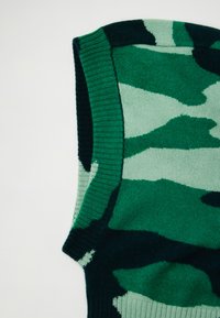 Zielony sweter w kamuflażu z dzianiny, który łączy różne odcienie zieleni, ma prążkowany dekolt i kontrastowe tekstury. Wykonany z miękkiego, elastycznego materiału.