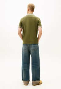 Oliwkowa koszulka polo z białym wykończeniem, zestawiona z szerokimi niebieskimi dżinsami i beżowym obuwiem. Gładki materiał i luźny krój.