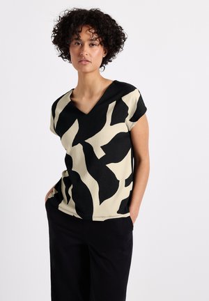 V-neck top with short sleeves, featuring an abstract black and cream pattern on a textured fabric. Worn with black trousers.