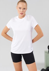 White short-sleeve performance t-shirt with moisture-wicking fabric. Paired with black fitted shorts, featuring a minimal logo detail.