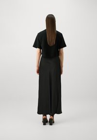 Un tricou negru scurt cu mâneci scurte, asortat cu o fustă lungă neagră, având o textură netedă și sandale cu toc pătrat.