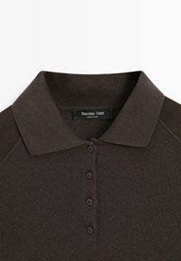 Brown polo shirt featuring a classic collar, button front, and ribbed texture. The fabric is smooth with contrasting shoulder accents.