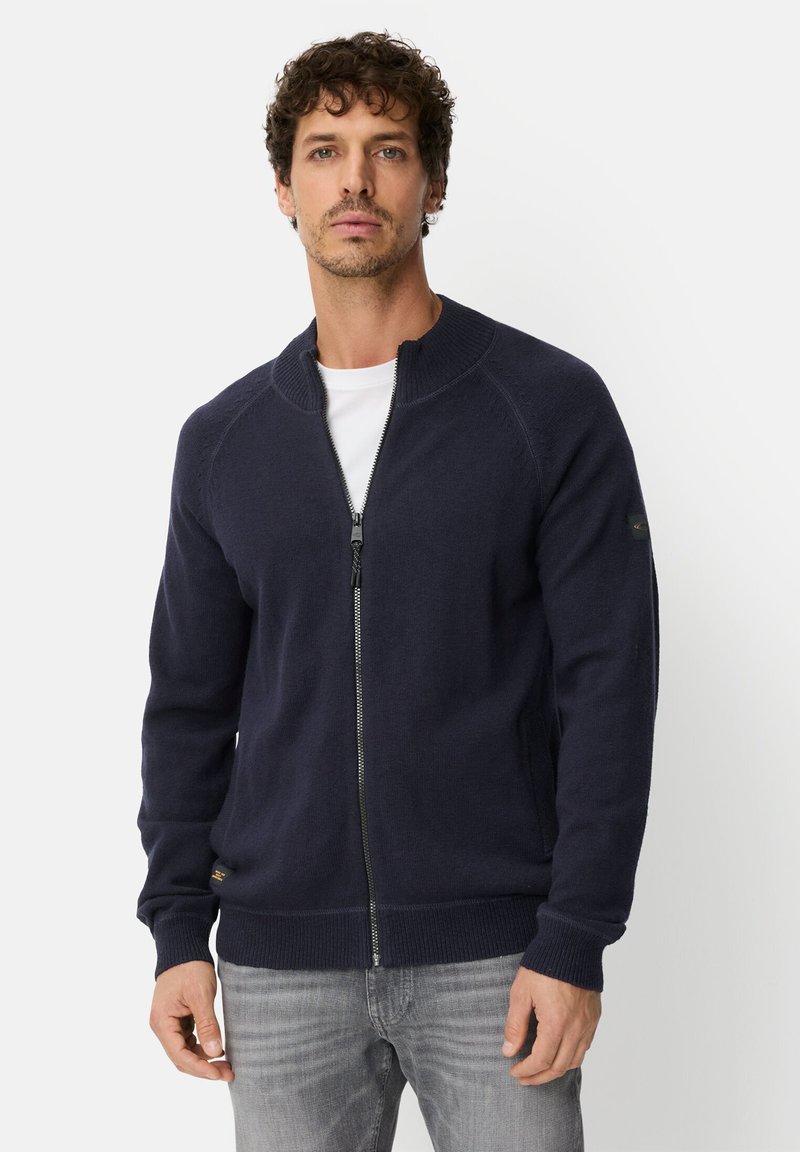 Navy zip-up knit cardigan with a high collar, ribbed cuffs and waistband, and a subtle logo accent on the sleeve. Soft texture.