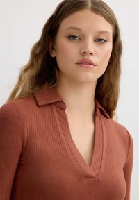 Top acanalado en rosa empolvado con escote en V y cuello. La tela es texturizada, y el diseño cuenta con mangas ajustadas y un acabado pulcro.