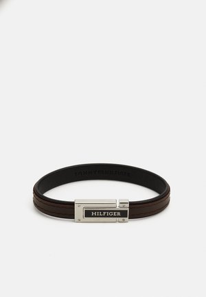 Braunes Lederarmband mit einem silberfarbenen Verschluss, einem schwarzen HILFIGER-Tag, strukturiertem Oberflächenfinish und zwei erhöhten Lederriemen.