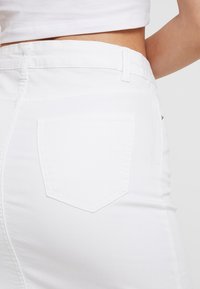 Jupe en jean blanche présentant une coupe ajustée, une texture subtile et une seule poche arrière de forme rectangulaire. Détail de taille standard.