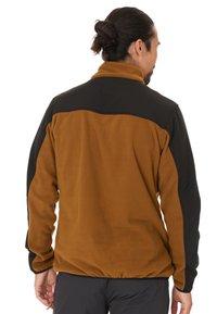 Fleecejacka som har en brun kropp med svarta axel- och nackdetaljer. Hög krage och elastiska ärmmuddar; mjuk textur med en avslappnad passform.