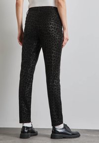 Pantalons en imprimé léopard noir avec une coupe slim, présentant une texture douce, une taille plate et des poches arrière. Assortis à des chaussures noires.