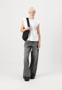 Cămașă albă fără mâneci, geantă de umăr neagră matlasată, blugi gri evazați și saboți negri. Design minimalist cu o croială casual și culori neutre.
