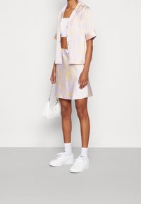 Tvådelat set i ljus lila med virvlar. Kortärmad knapp-up skjorta i kombination med en matchande A-linjeformad kjol. Vita sneakers och väska.