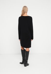 Abito lungo a maniche lunghe nero in maglia con scollatura a girocollo e polsini a costine, abbinato a stivali neri in pelle con tacco alti fino al ginocchio.