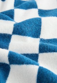 Vilnas sega ar pārbaudes rakstu, kurā mainās zila un balta kvadrāti. Mīksta tekstūra ar redzamām šķiedrām un nelielu piekārti.