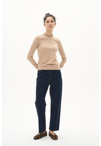 Beige neule, jossa on frillain kaula-aukko, yhdistettynä löysiin tummansinisiin farkkuihin ja leopardikuosisiiin ballerinoihin. Minimalistinen tausta.