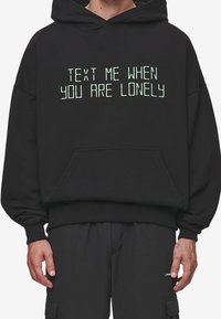 Black hooded sweatshirt featuring green text that reads "TEXT ME WHEN YOU ARE LONELY." Made of soft material with a spacious pocket.