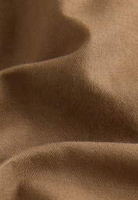 Gros plan sur des plis de tissu brun doux et texturé mettant en valeur son motif tissé et sa surface lisse.