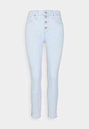 Jeans taille haute bleu clair avec une fermeture à cinq boutons sur le devant, coupe slim, légère déchirure au niveau de la cheville et sans poches visibles.