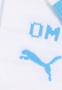 Bijela sportska čarapa s svijetloplave boje teksta i logom. Ima udoban, pleteni materijal s ojačanim dijelovima prstiju i pete.