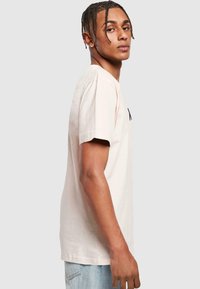 Lys pink bomulds t-shirt med korte ærmer, rund halsudskæring og en sort grafik på brystet. Båret med blå jeans.
