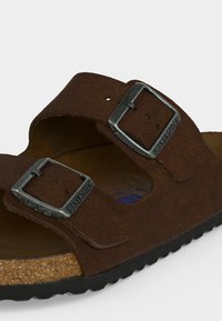 Καφέ σουέντ σανδάλι Birkenstock με δύο ρυθμιζόμενες μεταλλικές αγκράφες και φελλό πέλμα σε λευκό φόντο.