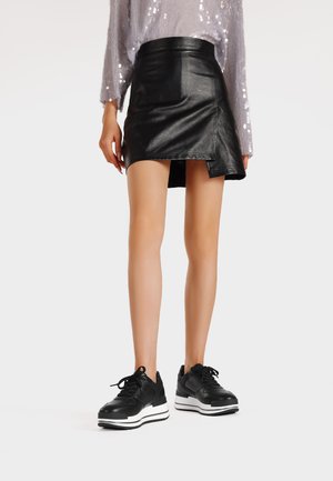 Mini gonna in pelle nera con orlo asimmetrico abbinata a sneaker nere chunky con suola bianca e lacci neri.