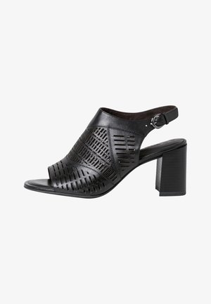 Black leather high-heeled shoe with cut-out geometric patterns, open toe, and ankle strap buckle. Features chunky heel and smooth texture.