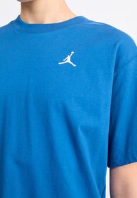 Modrá bavlněná trička s kulatým výstřihem a krátkými rukávy. Na levé části hrudi se nachází bílé logo Jumpman. Hladká textura.