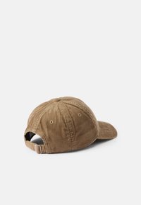 Brun kordflöjel baseballkeps med en böjd skärm, justerbart band och ventilationshål på baksidan. Tjock textur med ribbstruktur.