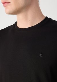 Zwarte katoenen t-shirt met ronde hals, voorzien van een klein, geborduurd cK-logo aan de linkerkant van de borst. Soepele textuur.