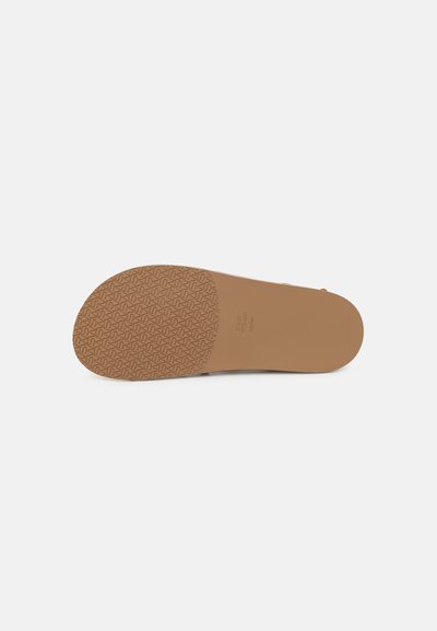 Semelle d'une sandale beige avec un motif antidérapant texturé sur la moitié avant et une surface lisse sur la moitié arrière sur fond blanc.