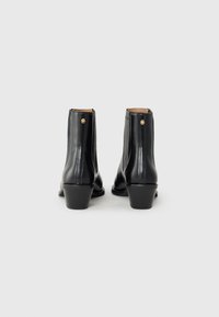 Bottines en cuir noir avec un petit talon, comprenant une fermeture éclair à l'arrière et des détails de couture subtils. Texture lisse avec une finition brillante.