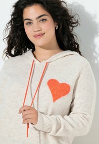 Maglione beige con cappuccio e un design a cuore arancione morbido sulla parte anteriore, con coulisse abbinata. Texture morbida, polsini a costine.