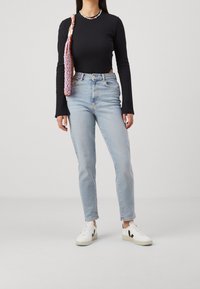 Kvinna i svart långärmad ribbad topp, ljusblå högmidjade jeans, vita sneakers och en rosa vävd axelväska.