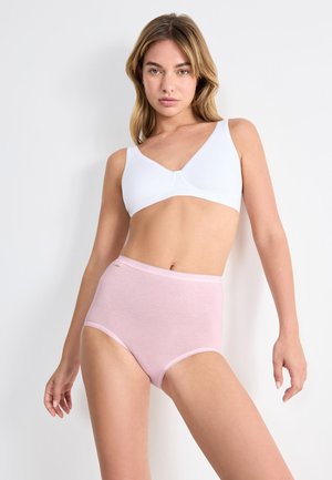 Donna che indossa un reggiseno wireless bianco e slip rosa chiaro a vita alta, in piedi contro uno sfondo bianco semplice.