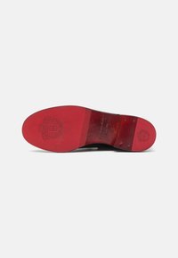 Talpa de pantof din piele neagră cu talpă din cauciuc roșu, având detalii gravate cu logo și accente texturate în zona călcâiului și degetelor.