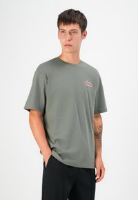 Grauer Kurzarm-T-Shirt aus weichem Baumwollstoff, mit einem kleinen bunten Grafikdesign auf der Brust und entspannter Passform; kombiniert mit einer schwarzen Hose.