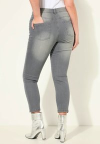 Vaqueros ajustados en denim gris con una cintura de media altura, bolsillos traseros y una pierna ceñida. Llevados con botines plateados de tobillo que cuentan con un tacón grueso.