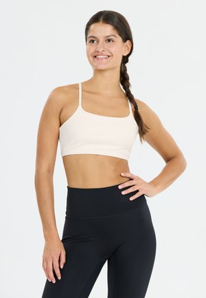 Soutien-gorge de sport beige clair avec des bretelles fines et un décolleté carré, associé à un legging noir taille haute, mettant en valeur un tissu lisse et extensible.