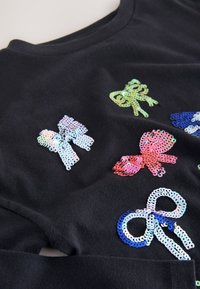 Črno blago s pisanimi pentljastimi apliciranimi bleščicami v različnih odtenkih, vključno z roza, modro in zeleno, ki dodajajo teksturo in podrobnosti.