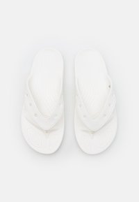 Valkoiset sandaalit, joissa on sormivälinen muotoilu, valmistettu joustavasta materiaalista. Muotoiltu pohja sisältää kuvioituja uria pitävää otetta varten.