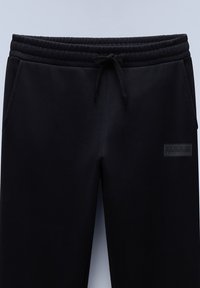 Zwarte sweatpants van zacht materiaal, met een elastische tailleband en een trekkoord, en een klein zwart logo op de zijkant.
