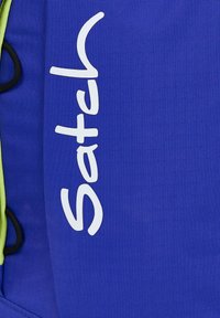 Blauer Rucksack aus strapazierfähigem Material mit einem auffälligen weißen "Satch"-Logo und grünen Akzenten, mit strukturiertem Oberflächen und verstellbaren Trägern.