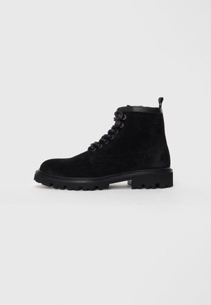 Black suede ankle boots with a rounded toe, lace-up front, metal eyelets, and a textured rubber sole. Includes a pull tab at the heel.